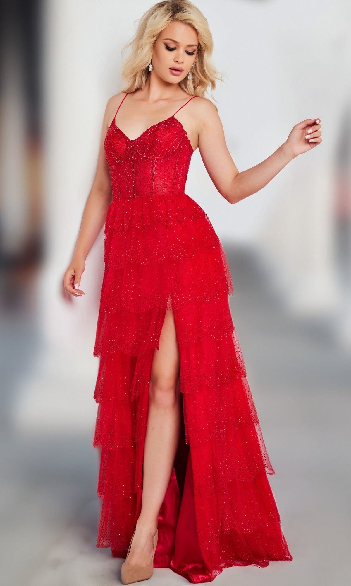 Woman wearing the Jovani Corset-Bodice Long Ruffled Prom Dress 38431, featuring spaghetti straps and a high slit, stands with one hand raised, looking down.