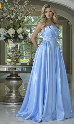 A woman models the Strapless A-Line Prom Ball Gown: Colors Dress 3845 in light blue, standing indoors beside a table with a floral centerpiece and candlesticks, her elegant gown reflecting classic formal style.