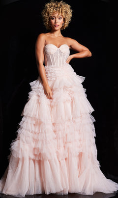 A woman with curly blonde hair wears the Jovani Ruffled Long Strapless Prom Ball Gown 38540 in light pink, featuring a fitted bodice and tiered pleated skirt, standing against a dark background.