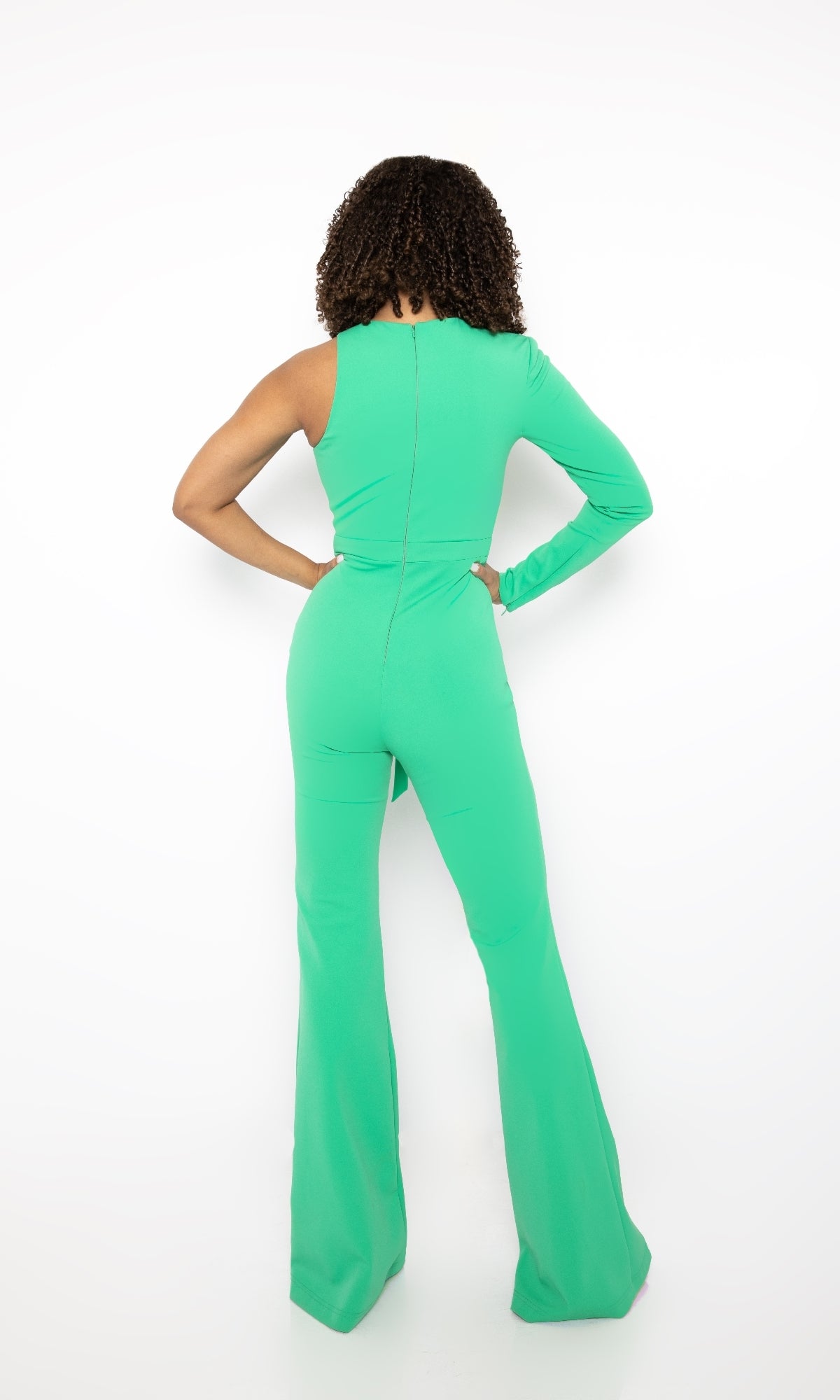 A person stands with their back to the camera, wearing the Ava Presley Long Formal Jumpsuit 38554 in bright green, featuring a round neckline and one long sleeve, set against a plain white background.