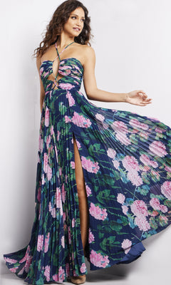 A woman poses in the Jovani Pleated Long Floral-Print Prom Dress 38638, featuring a strapless navy design, floor-length pleated skirt, bold floral print, and thigh-high slit as she holds one side of the dress out.