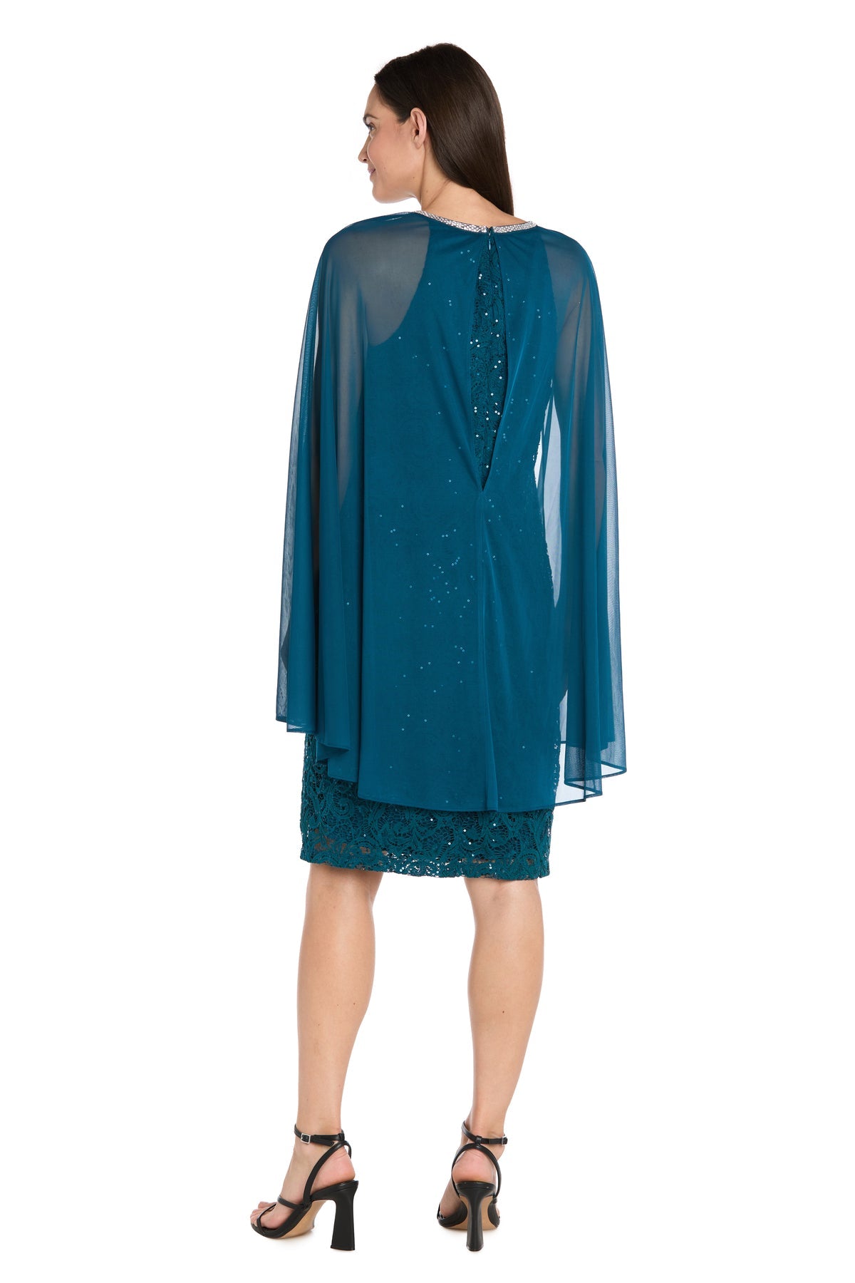 A woman faces backward in a teal Knee-Length Cape Party Dress: R&M Richards 3864, featuring a sheer cape overlay and black high-heeled sandals, set against a white background.