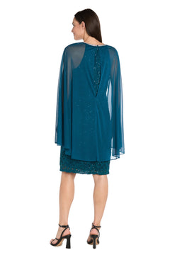 A woman faces backward in a teal Knee-Length Cape Party Dress: R&M Richards 3864, featuring a sheer cape overlay and black high-heeled sandals, set against a white background.