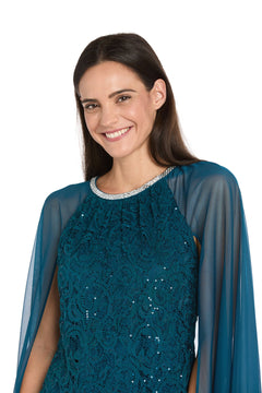 A woman with long brown hair smiles in the R&M Richards 3864 Knee-Length Cape Party Dress, featuring sheer sleeves and a decorative neckline, posing against a plain white background.