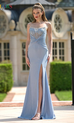 A woman in a dusty blue Beaded-Corset Long Prom Dress (Colors Dress 3867) with a strapless bodice and thigh-high slit stands outdoors in front of a building with round windows.