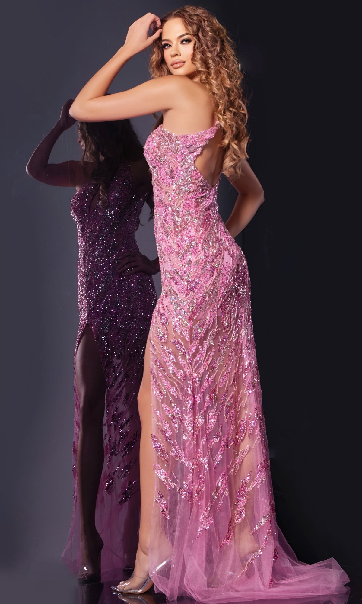 A woman wearing the Jovani 38769 long pink sequin prom dress, featuring a floor-length skirt and thigh-high slit, stands before a dark background with her reflection beside her.