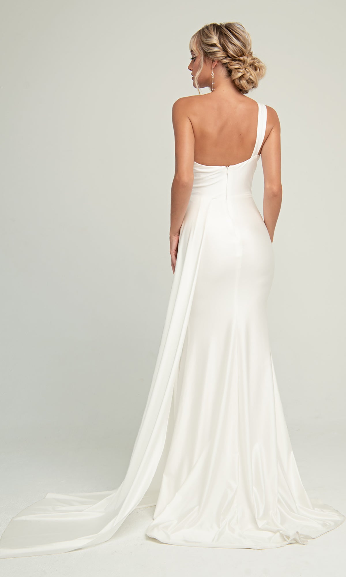 A woman wears the Side-Cape One-Shoulder Long Prom Dress 387, a fitted white gown with an Old Hollywood vibe and a small train, posing against a plain light background.