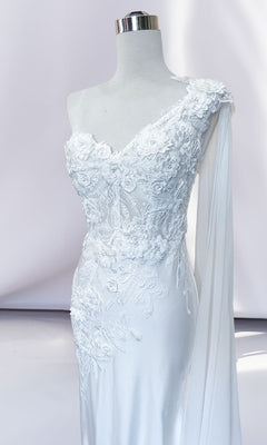 A white mannequin showcases the One-Shoulder Long Formal Dress with Cape 388, featuring a corset-style bodice, floral lace appliqué, and a draped sheer sleeve detail against a plain background.