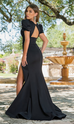 A woman poses outdoors near a stone fountain and lush greenery, wearing the Short-Sleeve Long Formal Dress 38868 with train—a black fitted evening gown featuring a high slit, open back, and puff sleeves.