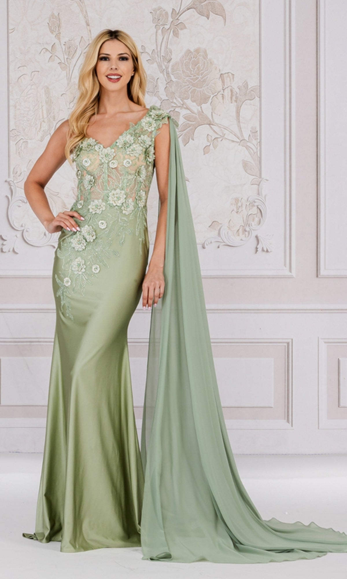 A woman poses against an ornate, light-colored wall in the One-Shoulder Long Formal Dress with Cape 388, featuring a flowing silhouette and elegant cape detail.