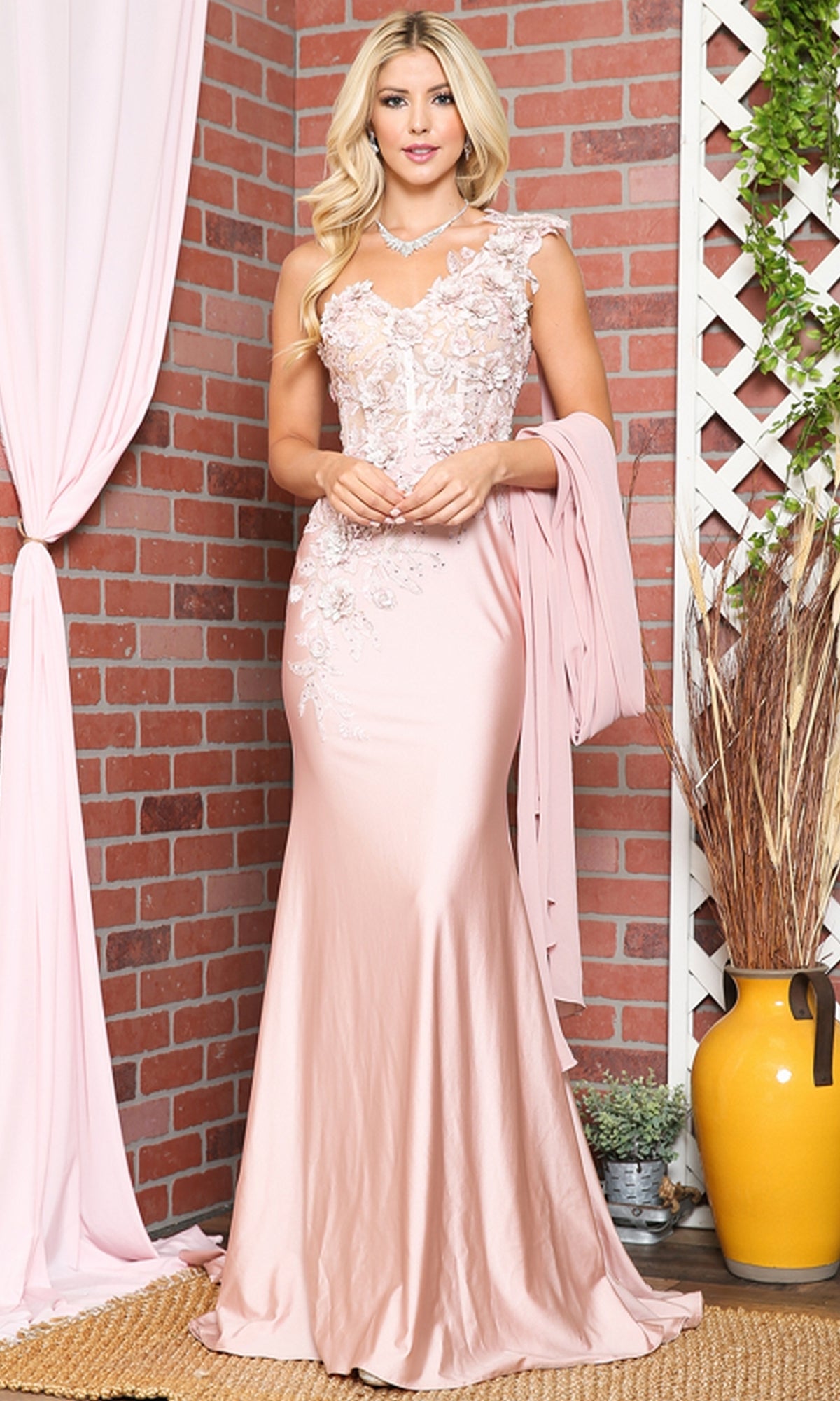 A woman stands indoors against a brick wall, wearing the One-Shoulder Long Formal Dress with Cape 388. She holds a matching cape, while decorative plants and drapes add sophistication to the elegant setting.