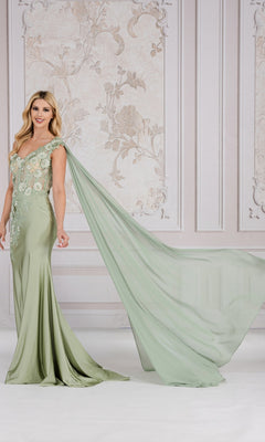 A woman wears the One-Shoulder Long Formal Dress with Cape 388, featuring a light green hue and floor-length design, as she stands before an ornate, light-colored wall.