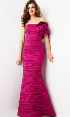 A woman poses against a plain white background wearing the Jovani 38947 long formal dress in fuchsia, featuring a fitted, strapless design with ruched texture and a prominent fabric flower detail on the left shoulder.