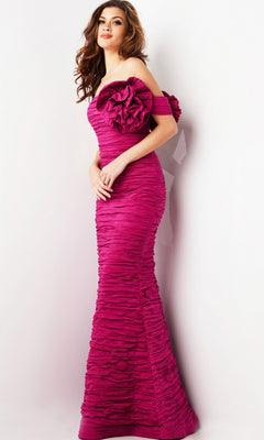 A woman stands against a plain white background wearing the Jovani 38947 long formal dress: a fitted, off-shoulder magenta designer gown featuring textured, ruched fabric and a large floral accent on the upper sleeve.