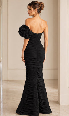 A woman in the Jovani 38947 long formal dress, styled with a fitted, ruched silhouette and a dramatic ruffled one-shoulder detail, stands in an elegant, neutral-toned room.