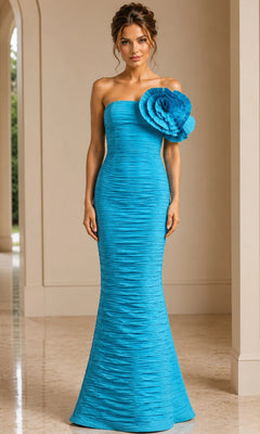 A woman stands indoors on a polished floor wearing the Jovani 38947 long formal dress in turquoise, featuring a strapless, textured design with a prominent floral detail on one shoulder.