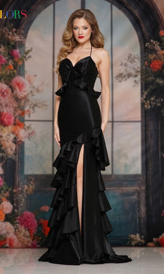 A woman in the black Sheer-Back Ruffle Prom Gown (Colors Dress 3899), featuring a sleeveless design and thigh-high slit, stands before an arched window with a floral backdrop.