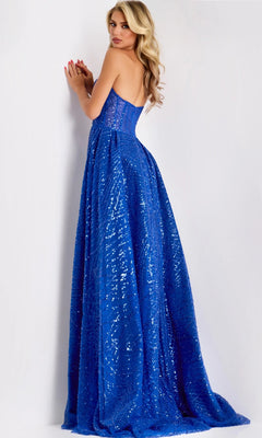 A woman with long, wavy blonde hair cascading down her back stands facing a wall and looks over her shoulder, wearing the Jovani 39029 long formal dress—a strapless, floor-length gown adorned with blue sequins.