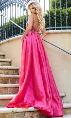 A woman with long blonde hair wears the Long Formal Dress: Jovani 39042 in bright pink as she stands on stone steps, glancing over her shoulder, with an iron fence and lush greenery behind her.
