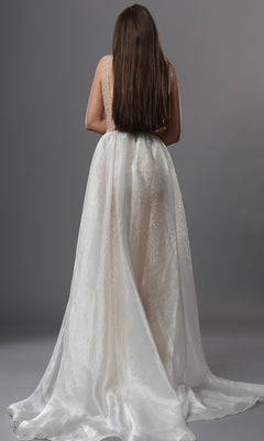 A woman with long brown hair stands facing away, displaying the flowing train of the Jovani 39043 long formal dress against a plain gray background.