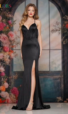 A woman in a black Cowl-Back Long Satin Prom Dress (Colors Dress 3906) with a thigh-high slit and strappy open back stands before a flower-decorated backdrop.