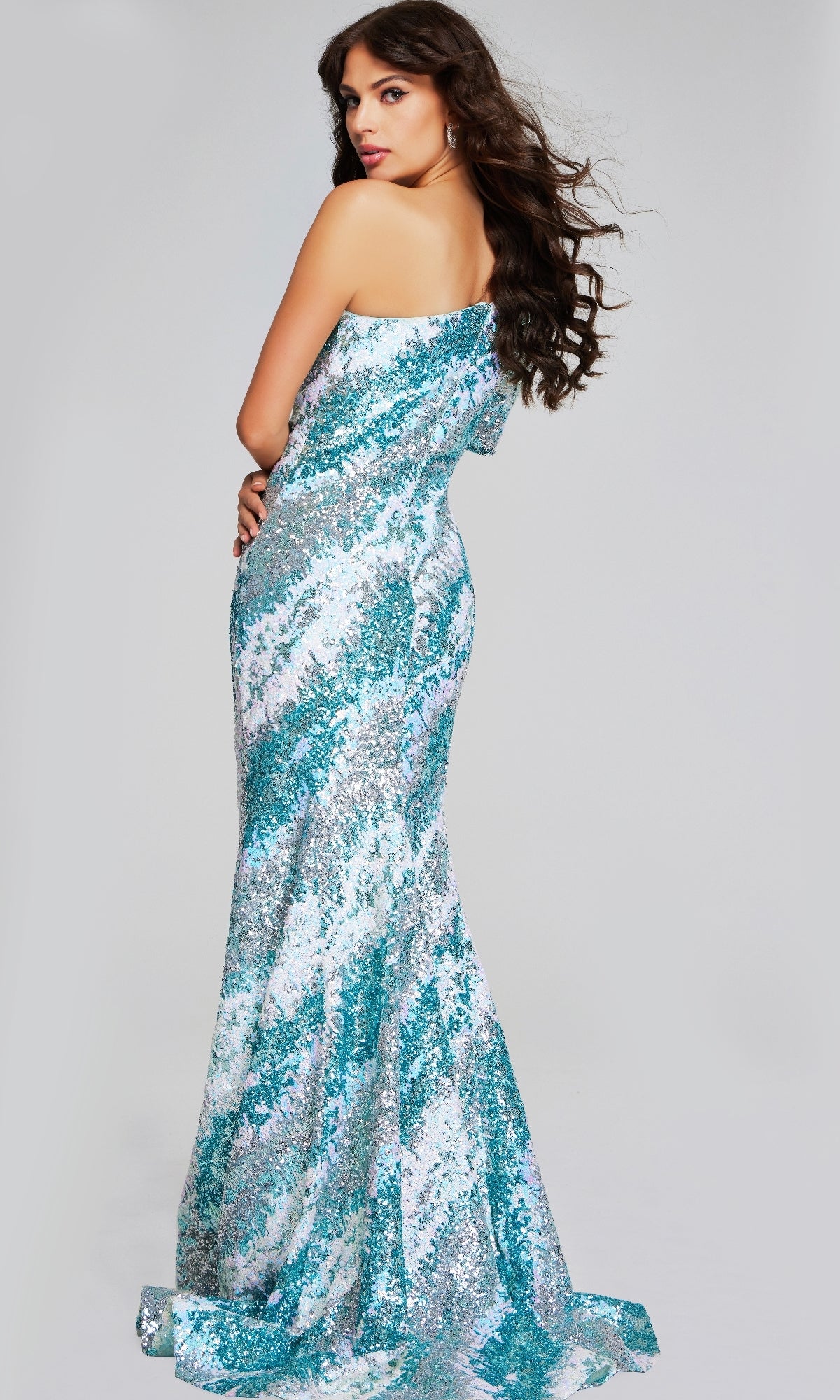 Woman wears the Jovani 39077 long formal dress, its shimmering blue and silver sequins catching the light as she poses with her back turned, glancing over her shoulder against a plain background.