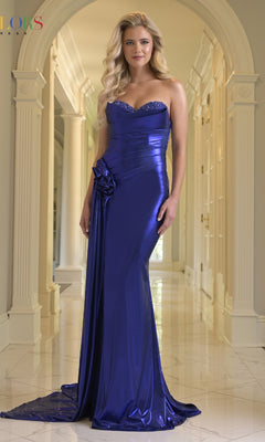 A woman in the Colors Dress 3910 long prom dress, featuring a metallic strapless design with an embellished bust and side detail, stands in an elegant hallway with arched doorways.