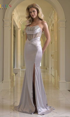 A woman stands in a hallway wearing the Beaded-Corset Satin Prom Gown: Colors Dress 3932 in silver, a fitted, floor-length gown featuring a thigh-high slit and stunning beaded corset detailing.