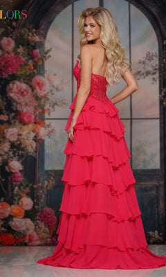 A woman with long blonde hair smiles in front of a floral, arched window backdrop wearing the Colors Dress 3934, a formal strapless long ruffled prom dress.