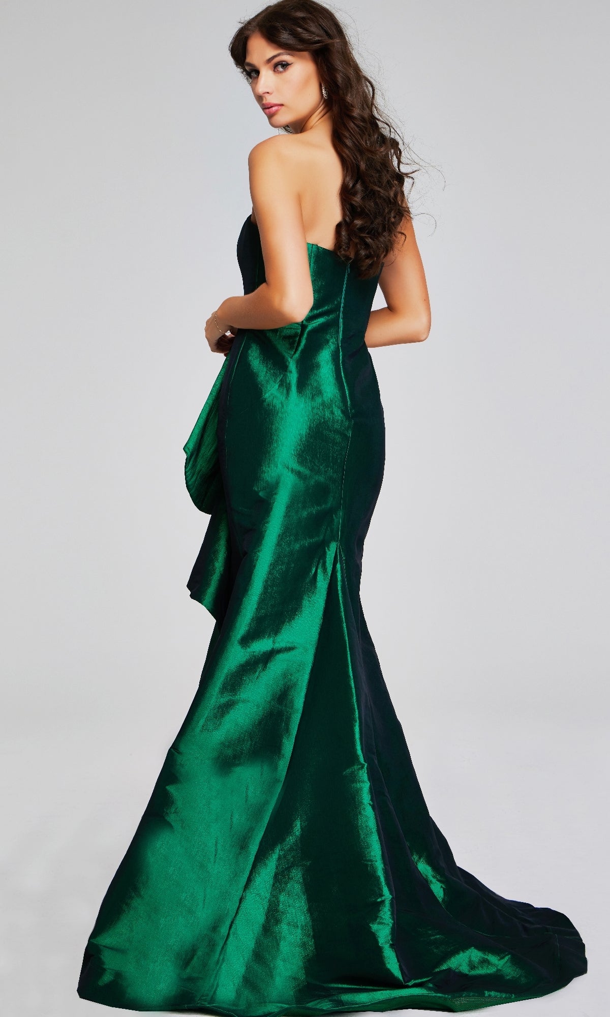 A woman poses with her back turned, glancing over her shoulder in the Jovani 39368 long formal dress against a plain light background.
