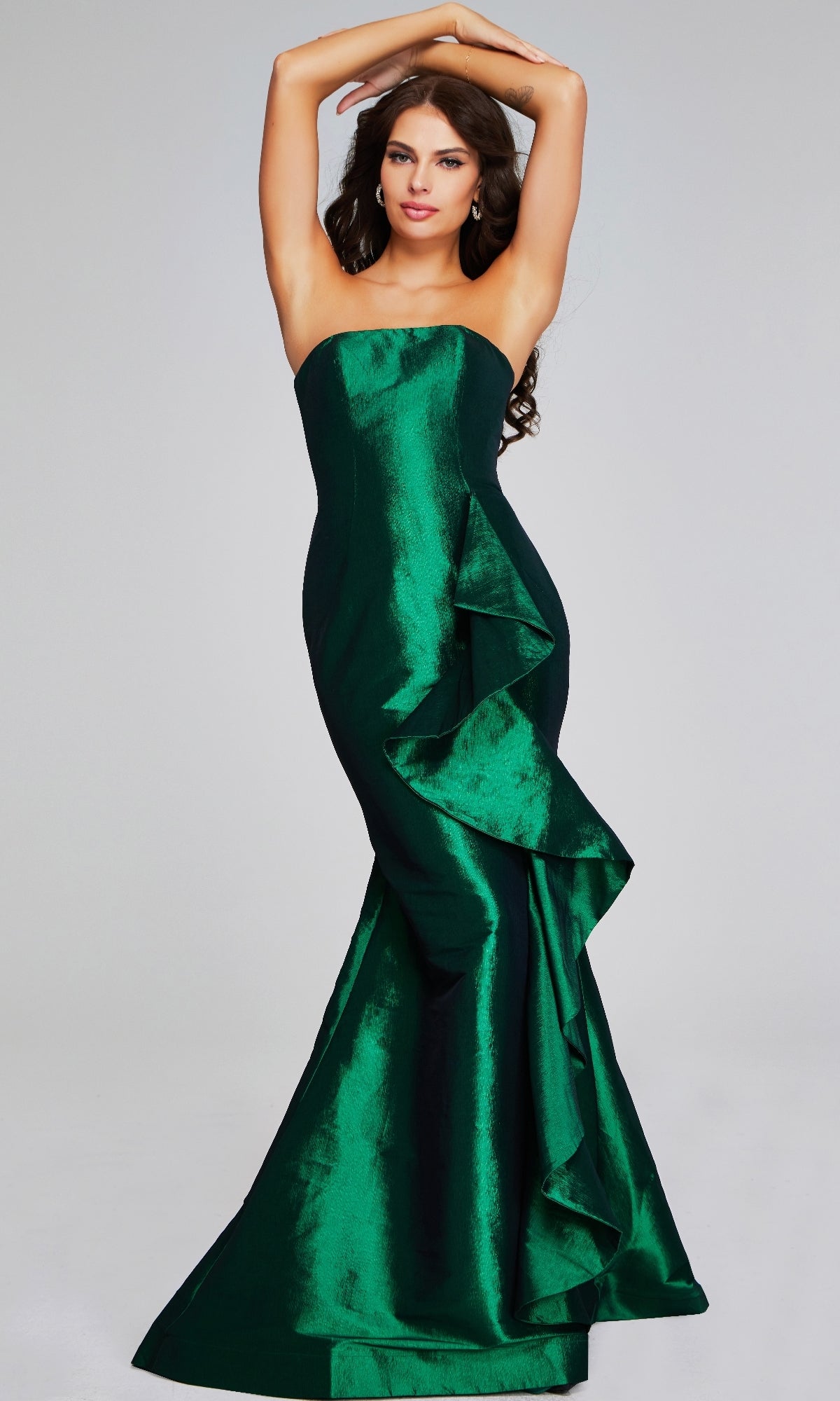 A woman models the Jovani 39368 Long Formal Dress, a strapless emerald green mermaid gown with a ruffled front detail, standing against a plain light background.