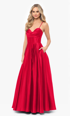 A woman models the Blondie Nites 3946BN Long A-Line Prom Dress—a floor-length, sleeveless red satin gown with thin straps, corset waist, fitted bodice, and pockets—against a plain white background.