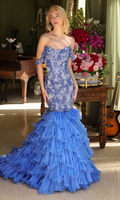 A woman wears the Long Prom Dress 39551 by Ava Presley, featuring embellishments and a layered ruffle skirt, standing indoors near a flower-adorned table with a guitar and piano in the background.
