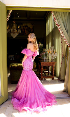 A woman wearing the Ava Presley 39570 Puff-Sleeve Long Prom Dress stands in a doorway, glancing over her shoulder in a beautifully decorated room with green curtains and a chandelier.