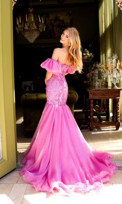 Wearing the Ava Presley 39570 puff-sleeve long prom dress with an embellished bodice, a woman stands indoors, facing away and glancing over her shoulder as sunlight pours through tall windows.