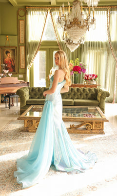 A woman in a light blue One-Shoulder Sequin Prom Gown (Ava Presley 39572) stands in a sunlit, elegant living room with green walls, a chandelier, and floral arrangements.