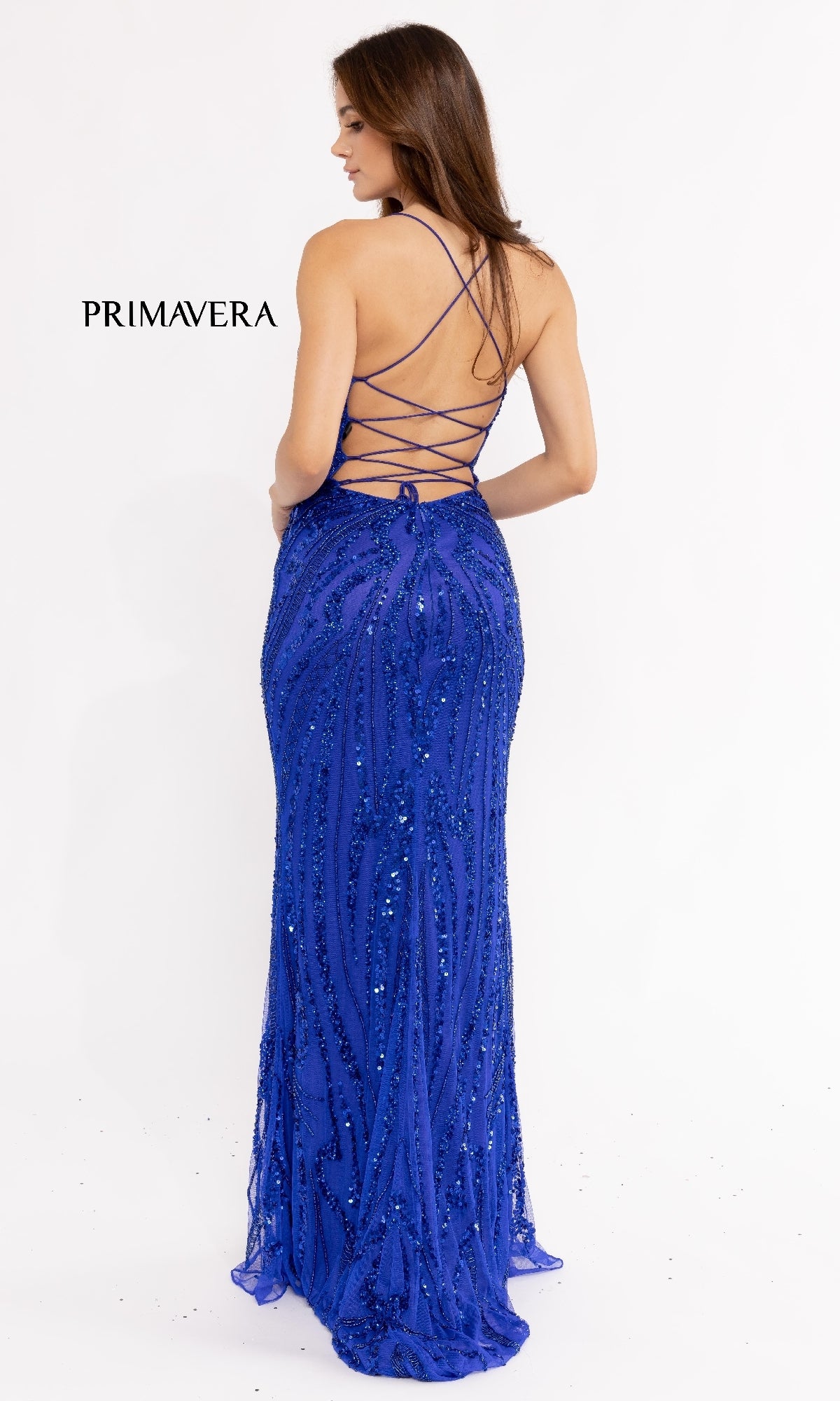 Woman in the Strappy-Back Long Sequin Prom Dress 3958—floor-length, royal blue with a crisscross lace-up open back—stands against a plain white background. 