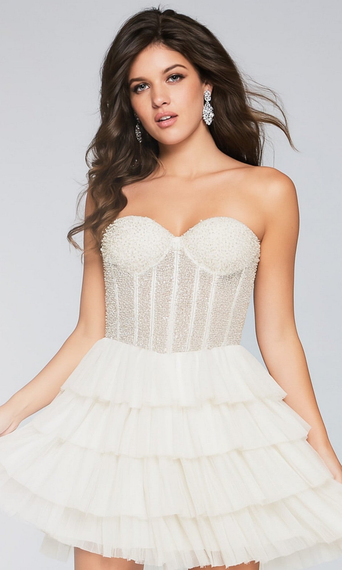 A woman poses against a plain background wearing the Jovani Short Strapless Homecoming Dress 39629 in white, featuring an embellished corset bodice and a layered, ruffled short A-line skirt.