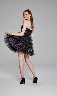 A woman wears the Short Black Glitter Hoco Dress: Jovani 39654 with high heels, posing against a plain gray background and smiling over her shoulder.