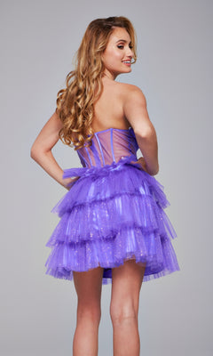 A woman with long wavy hair models the Jovani 39666 Strapless Short Glitter Hoco Dress, featuring a sheer corset waist and layered purple tulle, while standing and smiling over her shoulder.