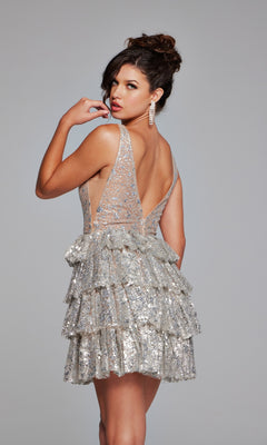A woman poses against a gray backdrop in the Ruffled Short Glitter Hoco Dress: Jovani 39700, a sleeveless silver sequined designer look with ruffled accents, turning partially to glance over her shoulder.