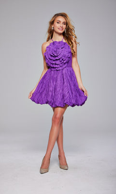 A woman stands in a studio wearing the Jovani 39741 Rosette Short Bubble Hoco Dress, a textured bright purple designer cocktail dress with ruffled flower details, paired with beige high heels.