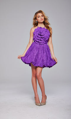 A woman poses in the Rosette Short Bubble Hoco Dress: Jovani 39741—a textured, sleeveless purple dress with circular ruffle details—paired with sparkly heels against a plain background.