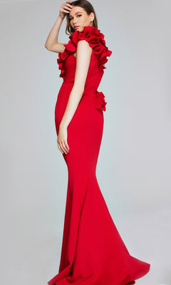 A woman poses against a plain light gray background wearing the Jovani 39751, a long formal fitted red mermaid gown with ruffled details on the shoulders and back.