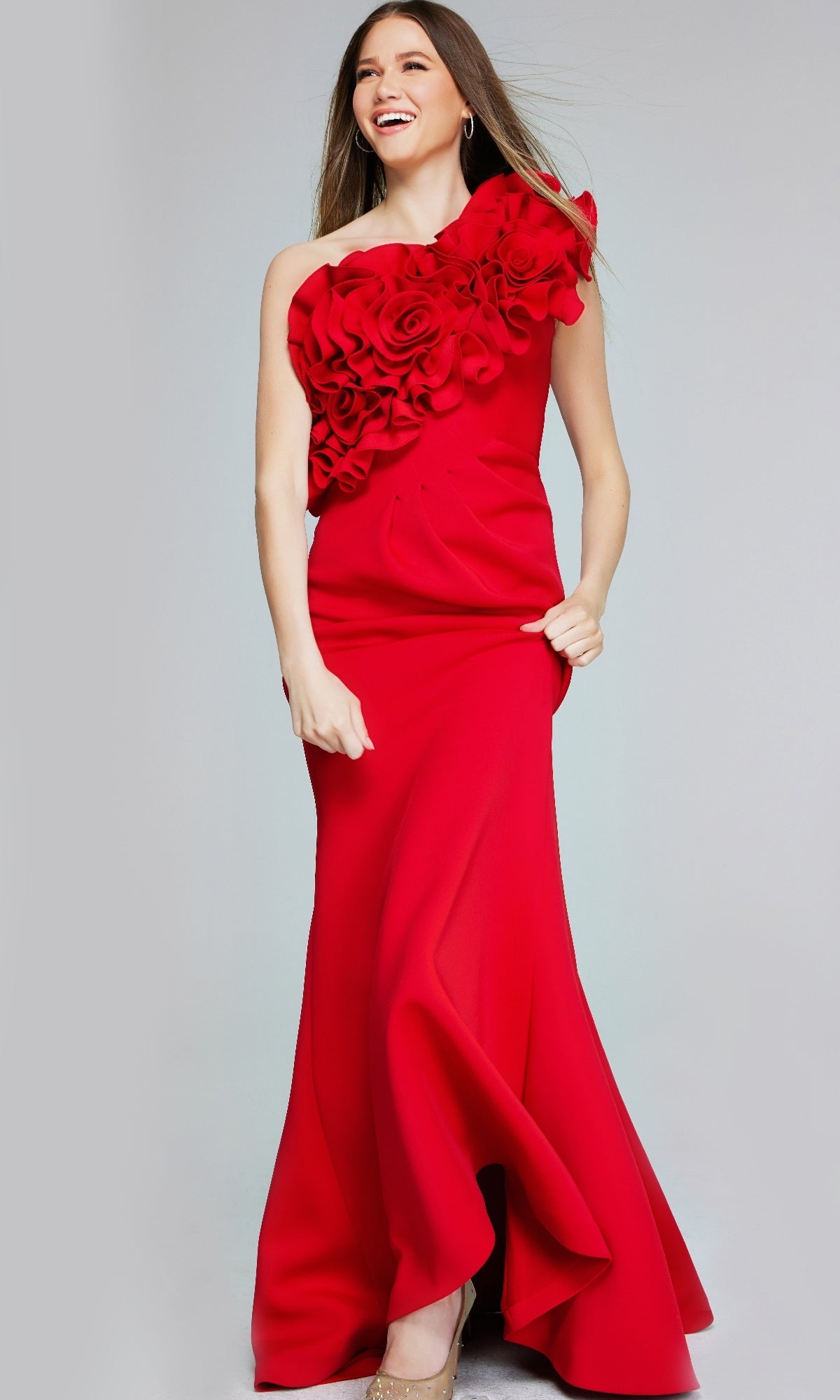 Woman wearing the Jovani 39751 long formal dress—a floor-length, bright red mermaid gown with one-shoulder floral applique—standing and smiling against a plain background.