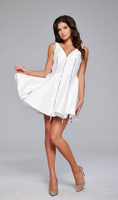 A woman in the Short A-Line Zipper Hoco Dress: Jovani 39821 and beige high heels poses against a gray background, holding out one side of her skirt.