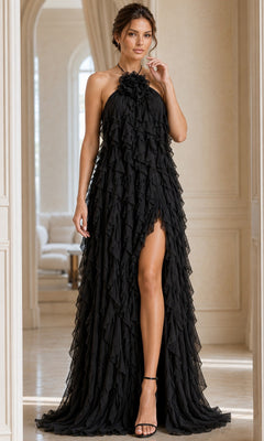 A woman stands indoors in a bright, sophisticated room wearing the Jovani 39823 Long Formal Dress in black—a sleeveless halter chiffon gown with ruffle layers, an elegant high slit, and a graceful A-line silhouette.
