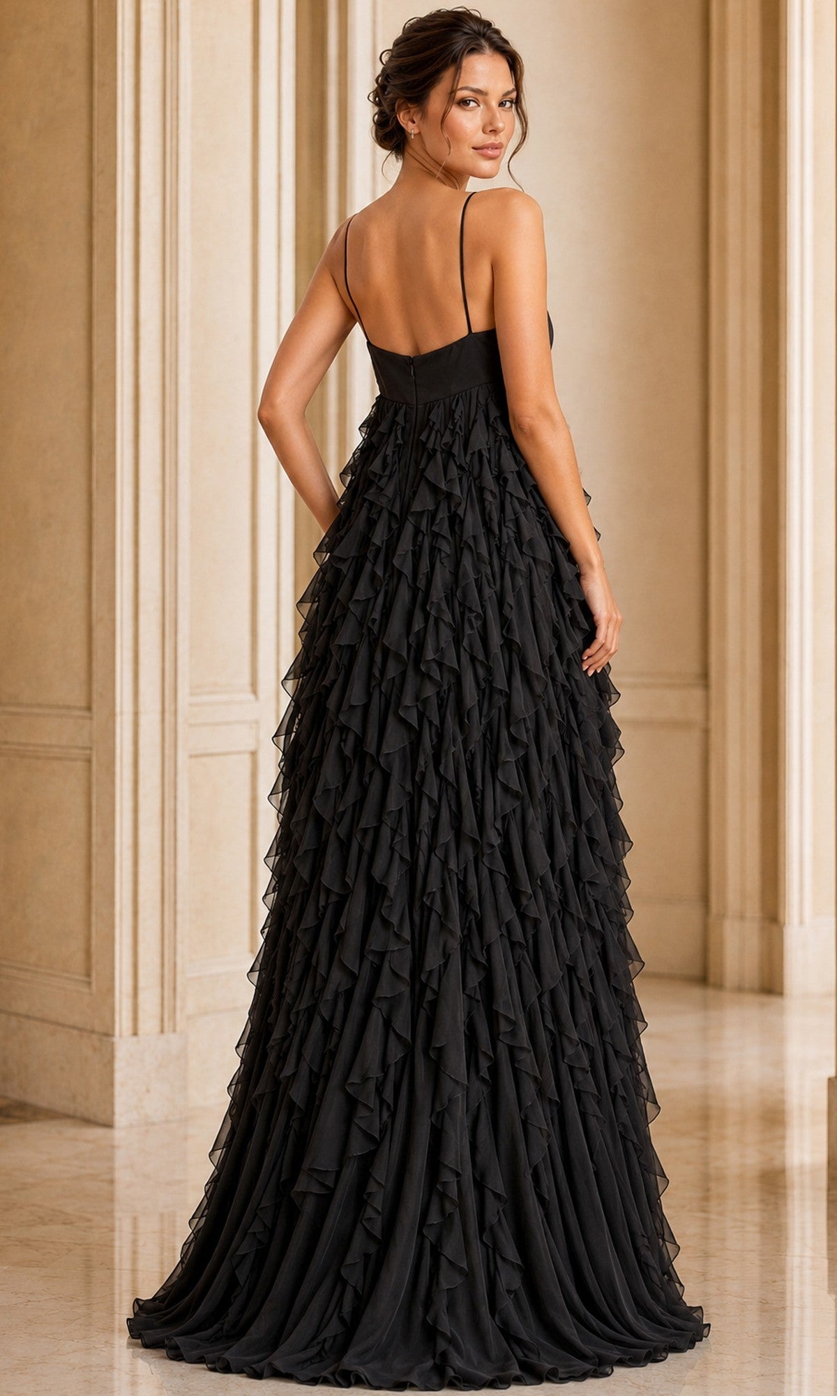 A woman stands indoors in the Jovani 39823 Long Formal Dress, a floor-length black gown with thin straps and elegant ruffle layers, looking over her shoulder. The scene is set against light-colored walls and marble flooring.