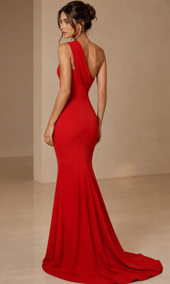 A woman wearing the Jovani 39971 long formal dress—a fitted, floor-length red mermaid gown with an open back—stands on a smooth beige floor, looking over her shoulder.