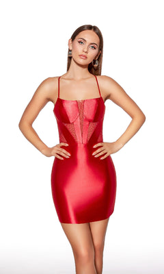 A woman stands confidently with hands on hips, wearing the Alyce 40018 Short Bodycon Corset Hoco Dress—a fitted, shiny red mini with thin straps and sheer panel accents—against a white background.